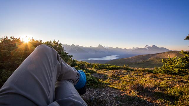 Shot of the photographer's legs as he sits and contemplates a mountain landscape in the background at sunrise in Jasper National Park.