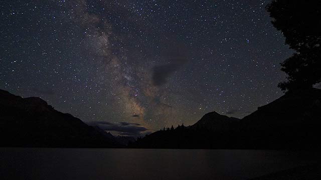 A starry sky over a lake with mountains in the background at Waterton Lakes National Park.