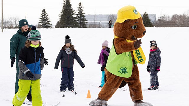 Children learning cross-country skiing accompanied by a beaver mascot.
