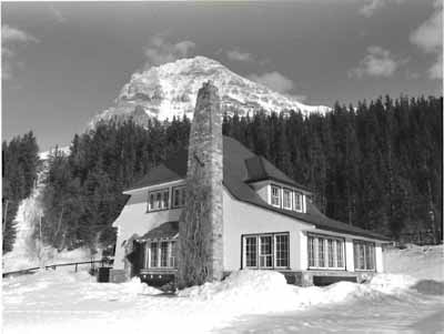 Side elevation of the Superindendent's Residence, showing the steeply pitched hipped-roof and massive, irregularly placed fieldstone chimney, ca 1965. © Agence Parcs Canada / Parks Canada Agency, ca./vers 1965.