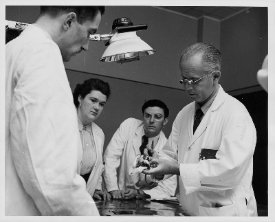 Historic photograph of Dr. Hans Selye demonstrating organ changes in a stressed rat during daily morning rounds, University of Montréal, May 1955. © Library and Archives Canada | Bibliothèque et Archives Canada