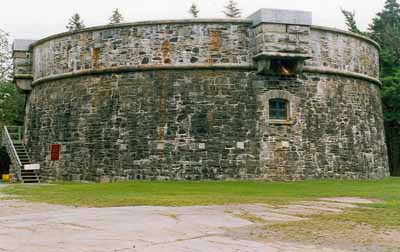 Vue générale de la Tour Martello Prince-de-Galles montrant les murs de maçonnerie circulaires massifs et le mur extérieur qui s’incline légèrement vers l’intérieur à mesure qu’il gagne en hauteur, 1995. © Parks Canada Agency / Agence Parcs Canada, 1995.