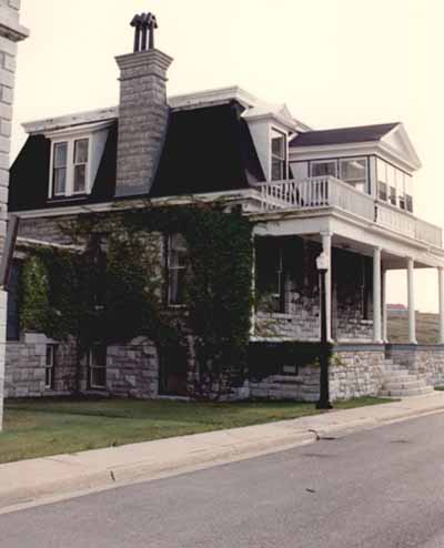 View of the front entrance of RMC Building 55, showing the prominent main elevation, with its broad and high porch, columns and stone staircase, 1993. © Parks Canada Agency / Agence Parcs Canada, 1993.