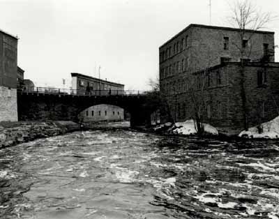 View of the East Mill, showing the four-storey massing and the two-storey adjoining addition, 1972. © Agence Parcs Canada / Parks Canada Agency, 1972.